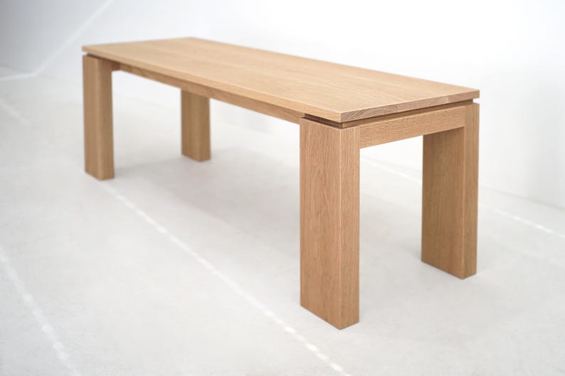 May include: A light wood bench with a rectangular top and four legs. The bench is made of solid wood and has a natural finish.