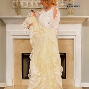May include: A cream christening gown with detailed lace and a matching bonnet. The gown has multiple fabric layers and delicate ruffles. The image includes the text "Royal Christening Gown".