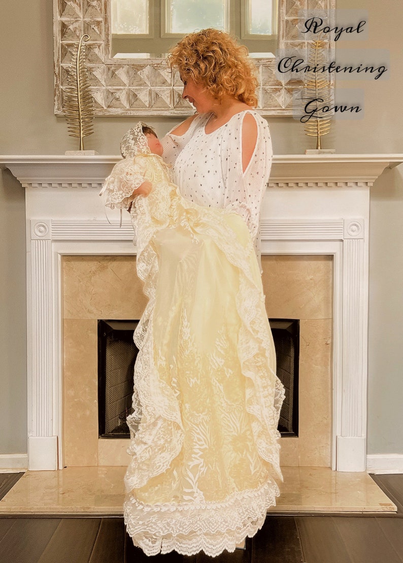 May include: A cream christening gown with detailed lace and a matching bonnet. The gown has multiple fabric layers and delicate ruffles. The image includes the text "Royal Christening Gown".