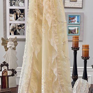 May include: A cream baptism gown with lace detailing and a rhinestone belt. The long, flowing gown features a floral pattern and is displayed on a hanger. A matching bonnet is also visible.