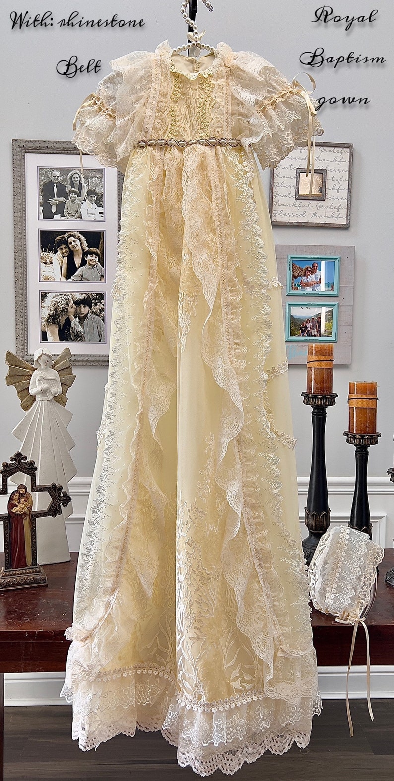 May include: A cream baptism gown with lace detailing and a rhinestone belt. The long, flowing gown features a floral pattern and is displayed on a hanger. A matching bonnet is also visible.