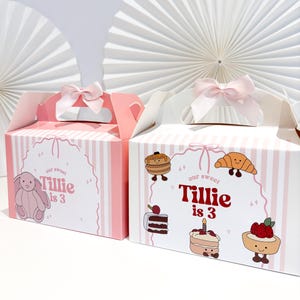 May include: Two pink and white striped gift boxes, each with a light pink bow. One box has a pink bunny illustration and the text "Tillie is 3". The other box features food illustrations and the text "Tillie is 3".