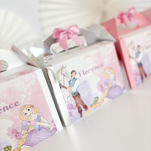 May include: A row of princess-themed gift boxes, each featuring illustrations of a princess and a prince. The boxes are pink and white with silver handles and pink bows. The name "Florence" is printed on the boxes.