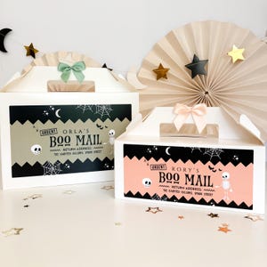 May include: Two white cardboard gable boxes with handles, each featuring a rectangular label with black zig-zag borders. The left box has a sage green label reading URGENT ORLA'S BOO MAIL, and the right box has a peach label reading URGENT RORY'S BOO MAIL.