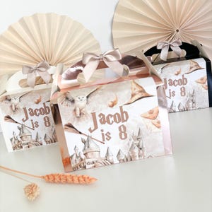 May include: Three party favour boxes with handles and bows. The boxes feature a castle illustration, a flying owl, and the text "Jacob is 8". The boxes are decorated with a light brown and white colour scheme.