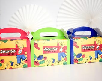 May include: Three colorful party favor boxes with red, green, and blue handles. Each box features a cartoon Lego figure and the text "Charlie is turning 6" on a yellow background with Lego brick graphics. White paper fans are in the background.