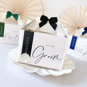 May include: Three white gift boxes with black ribbon bows and black text. The boxes are labelled "To the Groom", "To our Page Boy", and "Dougie".