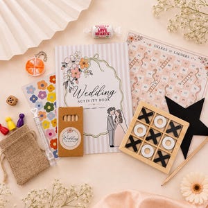 May include: A wedding activity book with a floral cover, a box of wedding crayons, a Snakes and Ladders game board, a wooden tic-tac-toe set with black and white pieces, a small burlap pouch, a bubble wand, colourful game pawns, and a Love Hearts sweet.