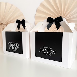 Pode incluir: Duas caixas de presente brancas com laços de fita preta. Uma caixa tem um rótulo preto com o texto "With love from Mr. & Mrs. Pursey 09.12.25". A outra caixa tem um rótulo preto com o texto "Thank you Jaxon 09.12.25".