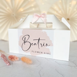 May include: White gift box with a pink ribbon and a pink and white label that says "Beatrix Flower Girl".