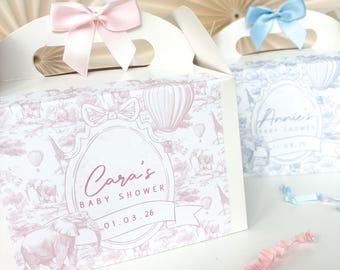 May include: Two white favor boxes with pink and blue bows. The boxes have a hot air balloon and animal print design. The pink box says "Cara's Baby Shower 01.03.26". The blue box says "Annie's Baby Shower".