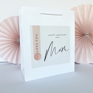 May include: White gift bag with a pink and white card that says "Happy Mother's Day Mom" with a pink wax seal that says "Love You".