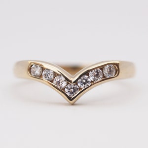 May include: A gold band ring with a V-shaped row of clear round diamonds.