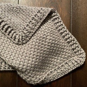May include: A gray crocheted blanket with a textured pattern. The blanket is folded in half and the edges are visible.