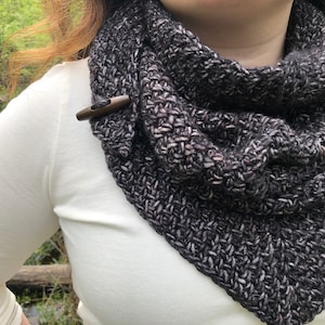 May include: A black and white knitted infinity scarf with wooden toggle closures. The scarf is worn around the neck and is a triangular shape.