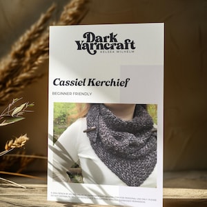 May include: A printable pattern for a beginner-friendly knitted scarf called the Cassiel Kerchief. The pattern is designed by Kelsea Wilhelm of Dark Yarncraft. The image shows a model wearing the finished scarf.