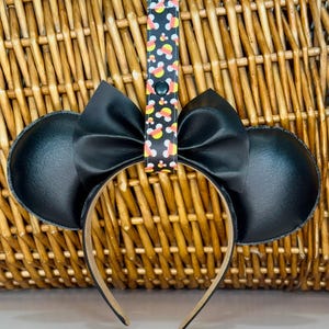 May include: Black headband with large black ears and a black bow. The headband has a candy corn print strap attached.