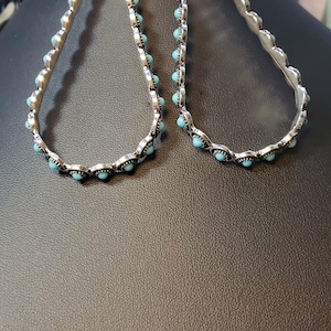 May include: Silver-toned earrings with a teardrop design. Each earring features a row of small, turquoise-colored stones along the edges and a larger turquoise stone at the top.