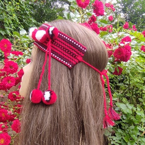 May include: A red and white crocheted headband with pom-poms. The headband is worn by a person with long brown hair.