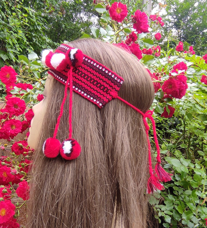 May include: A red and white crocheted headband with pom-poms. The headband is worn by a person with long brown hair.