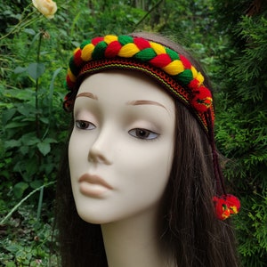 May include: A braided headband with red, yellow, and green yarn. The headband has tassels on the ends.