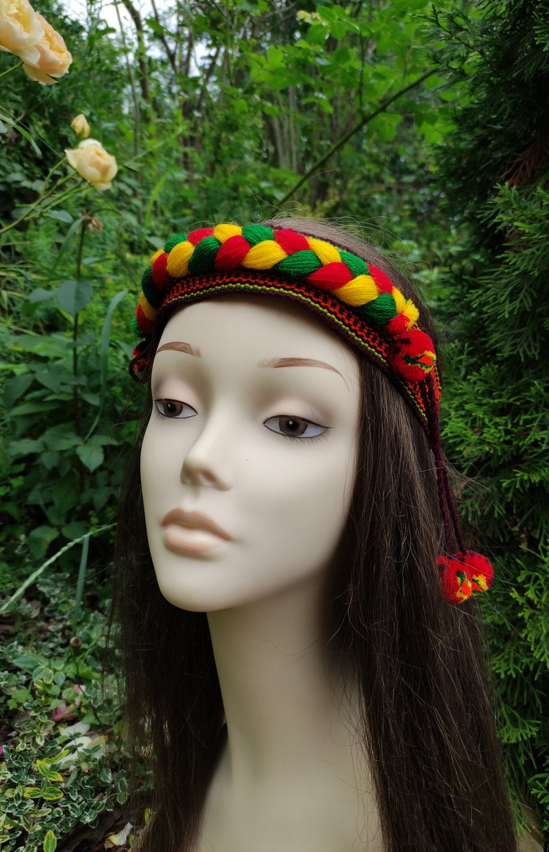 May include: A braided headband with red, yellow, and green yarn. The headband has tassels on the ends.