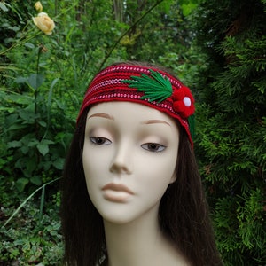 May include: A red headband with a green and white floral design. The headband is made of fabric and has a woven pattern.
