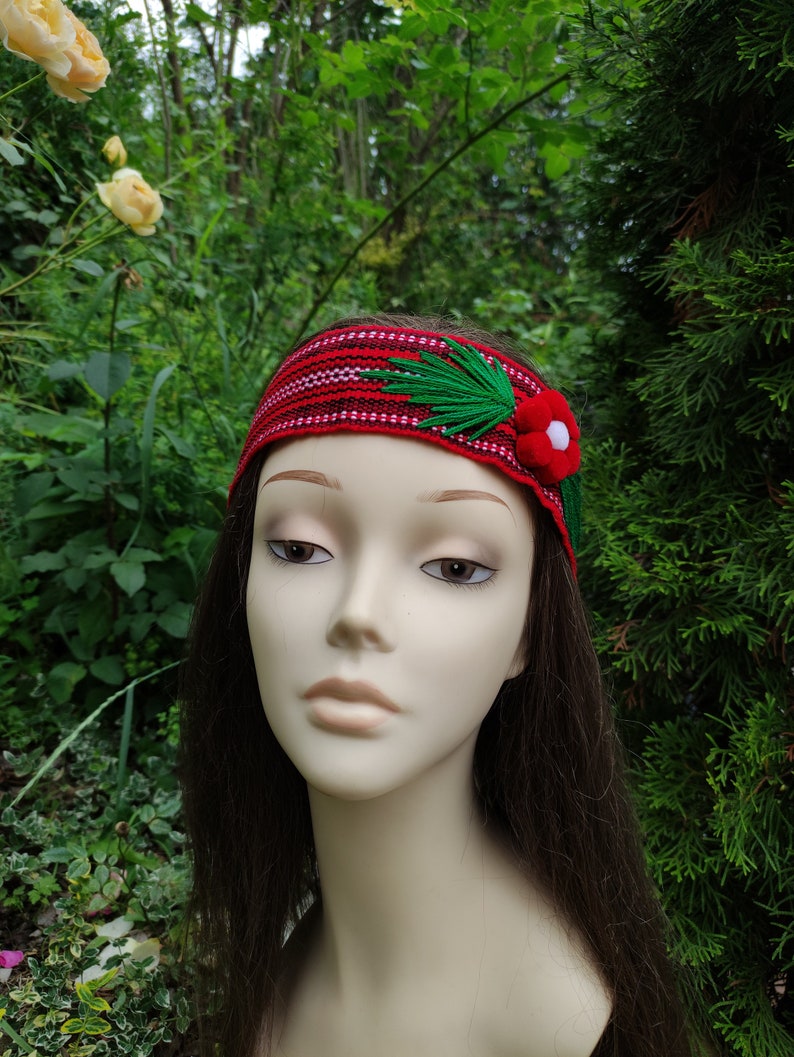 May include: A red headband with a green and white floral design. The headband is made of fabric and has a woven pattern.