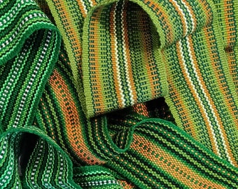 May include: Close-up of woven green, white, and orange ribbon. The ribbon has a striped pattern and is made of a soft, textured fabric.