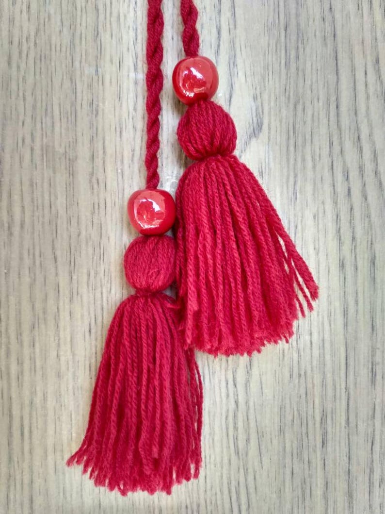 May include: Two red yarn tassels with red bead accents hanging from a wooden surface.