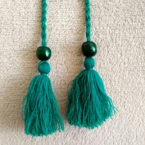 May include: Two green tassels with green beads at the top. The tassels are made of a soft, fuzzy material and are hanging from a white surface.
