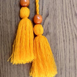 May include: Two yellow tassels with wooden beads hanging from a wooden surface.