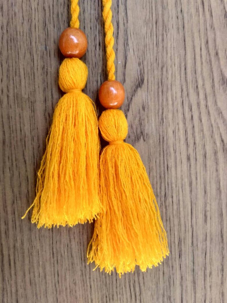 May include: Two yellow tassels with wooden beads hanging from a wooden surface.