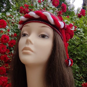 May include: A red and white braided headband with a white pom-pom on the end. The headband is worn by a mannequin with long brown hair.