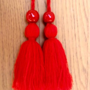 May include: Two red tassels with a red bead at the top of each tassel.