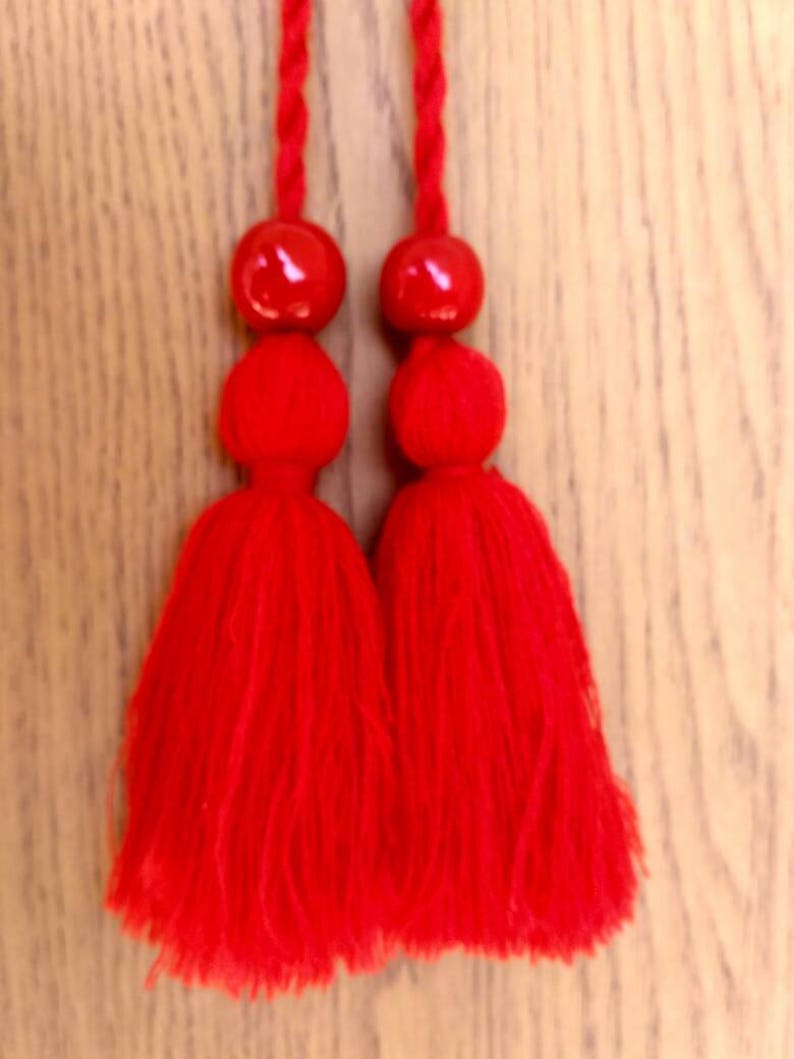 May include: Two red tassels with a red bead at the top of each tassel.