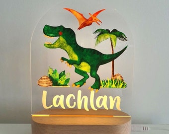 Puede incluir: Una luz nocturna de madera con un panel de acrílico transparente que presenta un dinosaurio verde, un dinosaurio naranja volador y una palmera verde. El nombre "Lachlan" está escrito en letras doradas en la base.