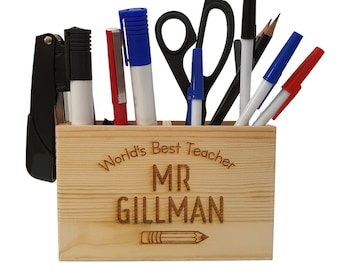 May include: Wooden desk organizer with compartments for pens, pencils, and other office supplies. It has an engraved message that says "World's Best Teacher MR GILLMAN" with a pencil icon.