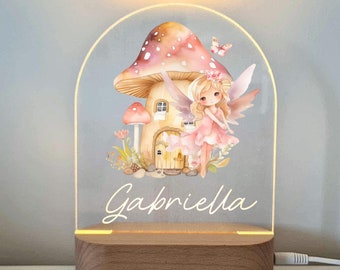 May include: A fairy-themed night light with a mushroom house and a fairy with wings. The light is on a wooden base and has the name "Gabriella" written on it.