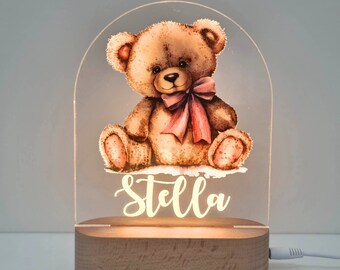 May include: A wooden base with a clear acrylic night light featuring a brown teddy bear with a pink bow. The name "Stella" is illuminated on the acrylic panel.