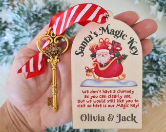 May include: A wooden Santa's Magic Key ornament with a gold-colored key attached. The ornament features a cartoon image of Santa Claus in his sleigh with a bag of gifts. The text on the ornament reads "Santa's Magic Key", "We don't have a chimney as you can clearly see, But we would still like you to visit so here is our Magic Key!" and "Olivia & Jack".