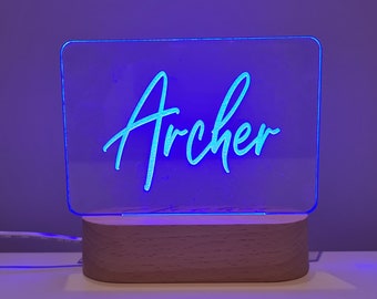 May include: A blue neon sign with the name "Archer" on a wooden base. The sign is lit up and the name is in a cursive font.