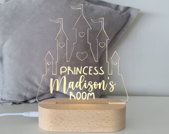 Puede incluir: Una luz nocturna de acrílico transparente con forma de castillo con letras doradas que dicen "Princess Madison's Room". La luz está sobre una base de madera.