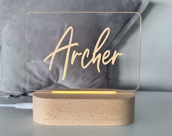 May include: A clear acrylic sign with the name "Archer" written in gold script on a wooden base with a warm white LED light.