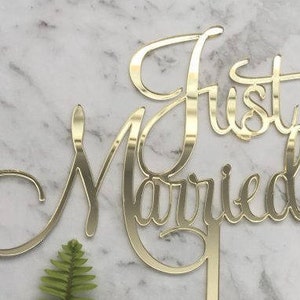 May include: Gold-coloured acrylic cake topper with the words "Just Married" in a cursive font.