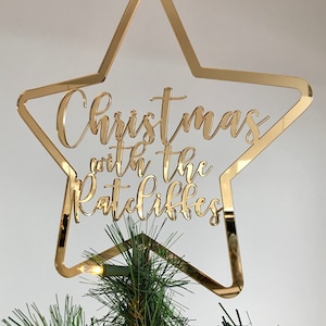 May include: Gold mirrored star Christmas tree topper with the text "Christmas with the Ratcliffes" written in cursive.