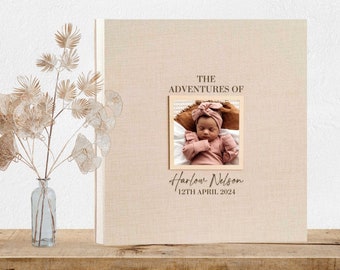 May include: A beige linen baby photo album with the text "The Adventures of Harlow Nelson 12th April 2024" and a photo of a baby girl in a pink outfit.