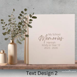 Puede incluir: Un álbum de fotos blanco con el texto "My School Memories" en una fuente cursiva. El texto "Hannah Kindy to Year 12 2023 - 2035" está impreso debajo del título.