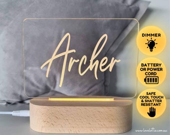 May include: A personalized acrylic night light with the name "Archer" in gold script. The light has a wooden base and a dimmer switch. It can be powered by battery or a cord. The light is safe to touch and shatter resistant.