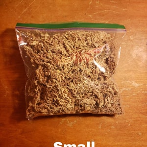 May include: A clear plastic bag filled with dried, light brown moss. The bag is sealed with a green zipper closure. The word "Small" is printed in white at the bottom of the image. The moss appears to be a natural product.